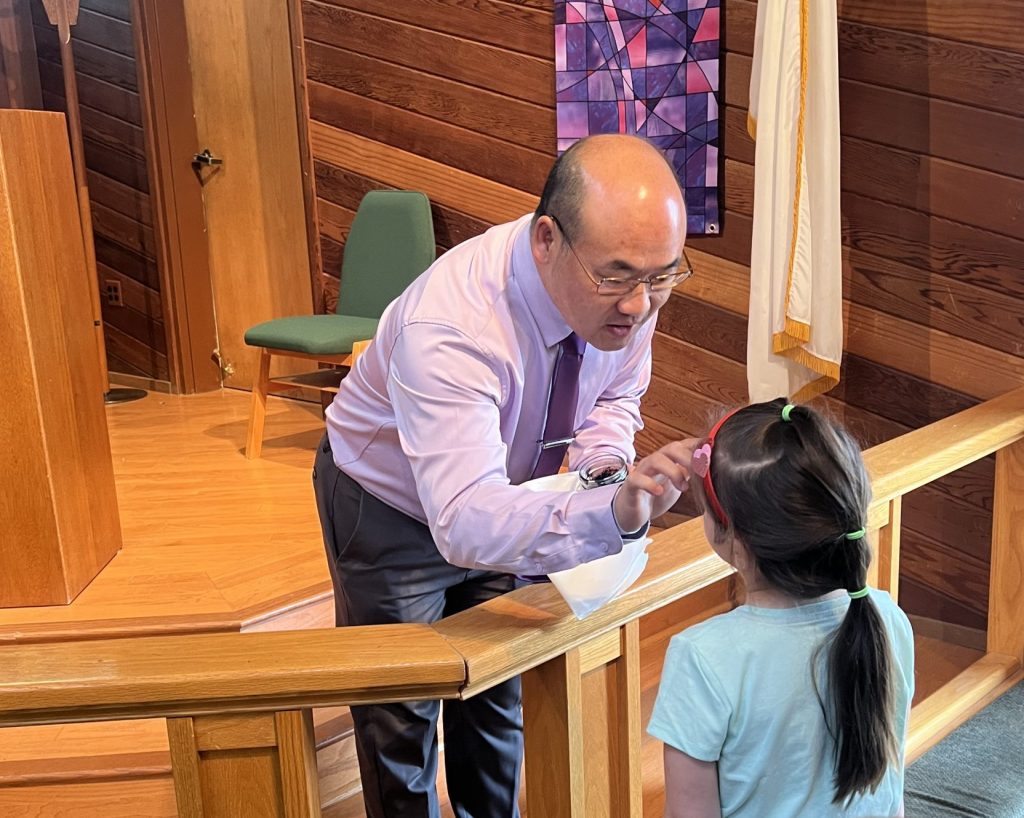 Pastor Doua leans forward to bless a student during Chapel service.