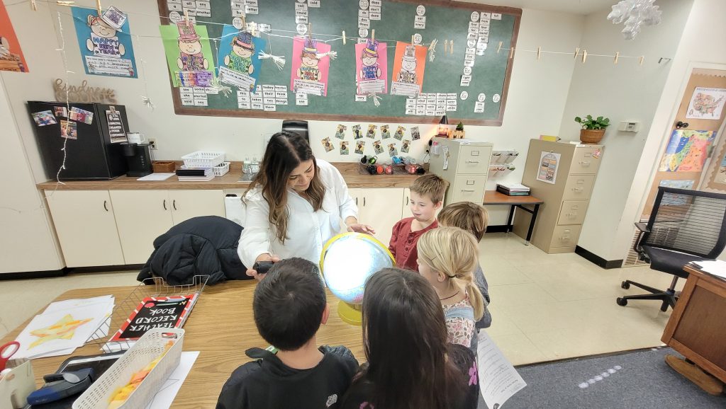 A teacher sits at a kidney-shaped table with a small group of five students to provide individual instruction.
