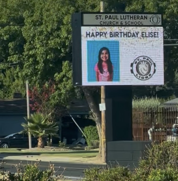A tall LED sign stands next to McKee Road displaying a birthday greeting for one of our students. The display shows the student's photo, school logo, and the words Happy Birthday!