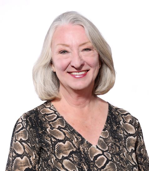 Melinda Price wears were platinum blonde hair in a classic styled bob. In this real estate portrait, she wears an earth-toned print blouse and is smiling widely. She's also the treasurer of St. Paul Lutheran Church's Mission and Ministry Board.