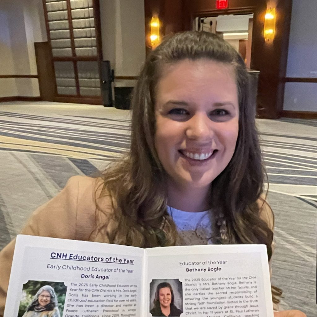 A brunette woman smiles toward the camera, holding a program open to an article featuring her photo.